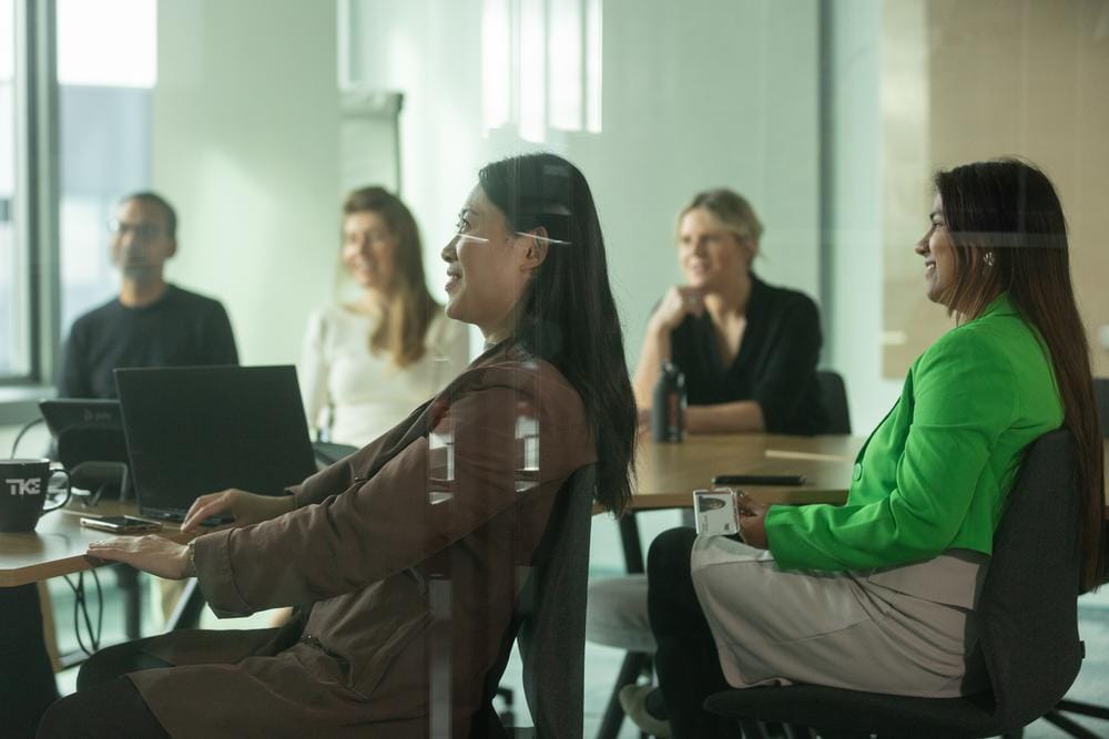 Colegas sorriem juntos ao redor de uma mesa de reunião com notebooks.