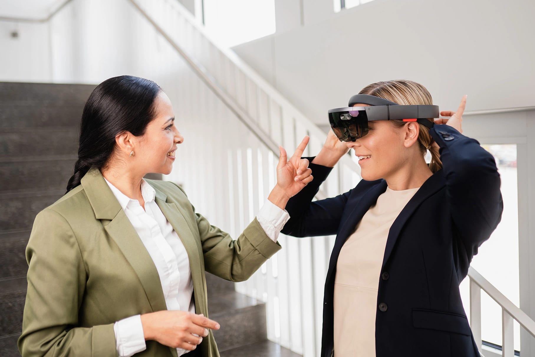 Duas colegas conversam em uma escada enquanto uma delas experimenta um headset de realidade mista.
